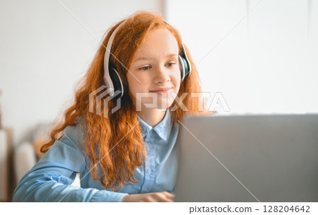 Distance Learning. Portrait of teeange schoolgirl having video lesson with laptop in living room at home, studying with computer during coronavirus quarantine, enjoying online education Distance Learning. Portrait of teeange schoolgirl having video lesson with laptop in living room at home, studying with computer during coronavirus quarantine, enjoying online education 128204642