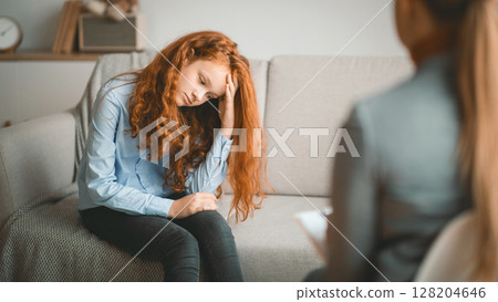 Child Psychologist. Worried sad teen girl having session with doctor or school teacher, grabbing head, sitting on the couch at office or home, thinking about her problems, feeling stress Child Psychologist. Worried sad teen girl having session with doctor or school teacher, grabbing head, sitting on the couch at office or home, thinking about her problems, feeling stress 128204646