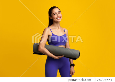 Yoga, Fitness, Pilates And Female Workout. Cheerful Positive Young Lady In Sportswear Holding Gray Mat For Training, Posing Isolated On Orange Background, Studio Shot. Wellness And Wellbeing 128204665