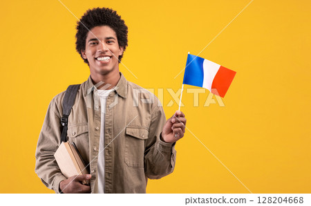 Language learning, student exchange, education and travel in new country. Young happy african american guy with backpack holds books and small France flag, isolated on beige background, studio shot Language learning, student exchange, education and travel in new country. Young happy african american guy with backpack holds books and small France flag, isolated on beige background, studio shot 128204668