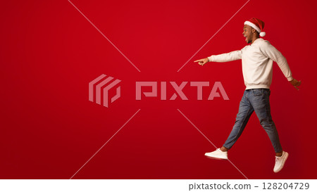 Check This. Excited Black Guy In Santa Hat Pointing Aside At Copy Space While Jumping On Orange Background, Showing Free Place For Your Xmas Offer Or Advertisement, Full Length Shot, Side View Check This. Excited Black Guy In Santa Hat Pointing Aside At Copy Space While Jumping On Orange Background, Showing Free Place For Your Xmas Offer Or Advertisement, Full Length Shot, Side View 128204729
