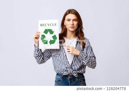 A woman holds a recycling sign, emphasizing the importance of eco-friendly habits. She is dressed casually and engages viewers in a sustainable conversation, likely in an indoor environment. A woman holds a recycling sign, emphasizing the importance of eco-friendly habits. She is dressed casually and engages viewers in a sustainable conversation, likely in an indoor environment. 128204778