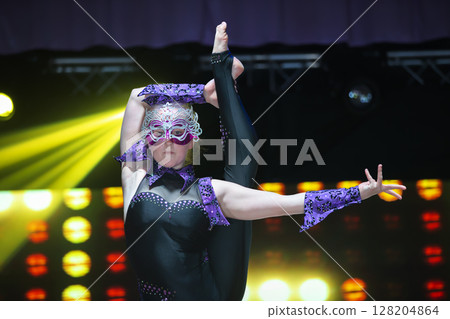 A girl equilibrist with a flexible body shows a difficult number on stage. A girl equilibrist with a flexible body shows a difficult number on stage. 128204864