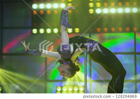 A girl equilibrist with a flexible body shows a difficult number on stage. A girl equilibrist with a flexible body shows a difficult number on stage. 128204869