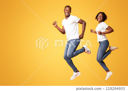Loving african american couple young man and woman smiling at camera and running in the air, copy space, orange studio background. Happy black lovers having sporty lifestyle, jogging together Loving african american couple young man and woman smiling at camera and running in the air, copy space, orange studio background. Happy black lovers having sporty lifestyle, jogging together 128204933