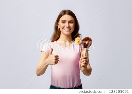 Cheerful Millennial Woman Demonstrating Natural Brushes For Eco Cleaning And Showing Thumb Up, Smiling Young Lady Recommending Plastic Free Items For Domestic Chores,Standing On Grey Background 128205091