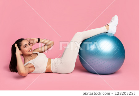Body Shaping Workout. Smiling Sporty Young Woman In Sportswear Doing Side Crunches With Legs On Blue Fitness Ball Isolated Over Pink Studio Background. Full Length, Banner. Pilates And Warm Up Concept Body Shaping Workout. Smiling Sporty Young Woman In Sportswear Doing Side Crunches With Legs On Blue Fitness Ball Isolated Over Pink Studio Background. Full Length, Banner. Pilates And Warm Up Concept 128205255