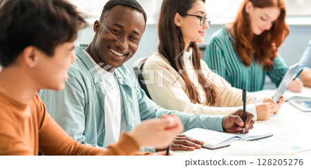 Friendship, Education And Teamwork Concept. Smiling international students sitting at table in public library and talking, doing homework together after classes, writing notes in notepad 128205276