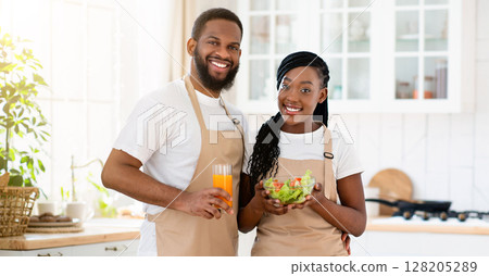 Vegan Family. Happy Black Couple With Fresh Vegetable Salad And Orange Juice Posing In Kitchen Interior, Young African American Spouses Enjoying Healthy Lifestyle And Tasty Food, Free Space 128205289