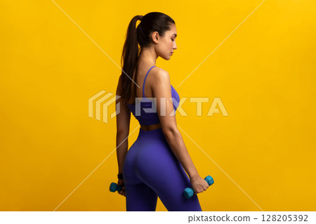 Training Concept. Portrait Of Determined Lady In Blue Sportswear Holding Two Dumbbells In Hands Posing Isolated Over Orange Studio Background, Showing Back. Sport, Motivation, Strength 128205392