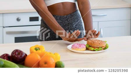 No Junk Food. Black Female Gesturing Stop To Donut And Burger Refusing To Eat Unhealthy Standing In Kitchen At Home. Nutrition, Harm Of Fastfood, Healthy Eating Choice No Junk Food. Black Female Gesturing Stop To Donut And Burger Refusing To Eat Unhealthy Standing In Kitchen At Home. Nutrition, Harm Of Fastfood, Healthy Eating Choice 128205398