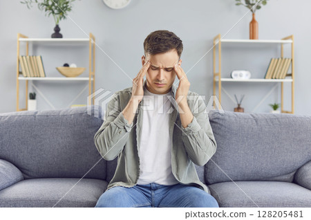 A man sits on the couch at home and has a headache A man sits on the couch at home and has a headache 128205481