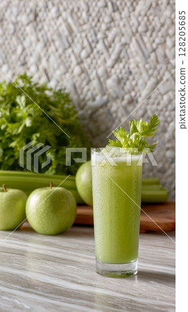 Fresh green juice in a glass with celery garnish and green apples on a marble countertop Fresh green juice in a glass with celery garnish and green apples on a marble countertop 128205685