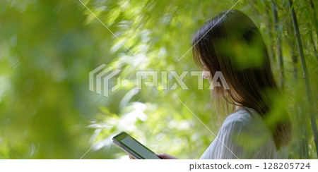A teen is reading on a tablet surrounded by lush green foliage, creating a serene atmosphere for relaxation and digital engagement 128205724