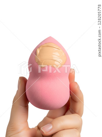 Pink makeup sponge with liquid foundation in hand, beauty blender isolated on transparent background, cosmetic application, flawless skin, blending tool 128205778