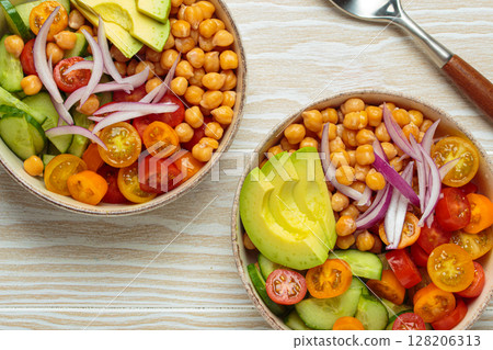 Two bowls with vibrant vegetarian chickpea salad with fresh vegetables in ceramic bowls top view 128206313