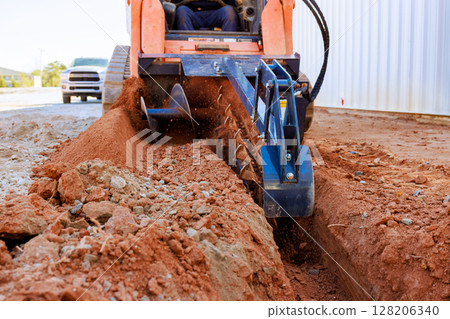 Worker operates trencher to dig trench in ground for construction purposes 128206340