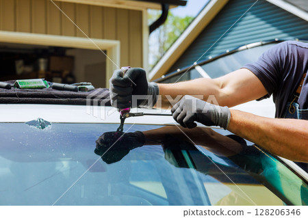 Technician uses specialized tools to removing damaged windshield on vehicle in auto repair shop garage. 128206346
