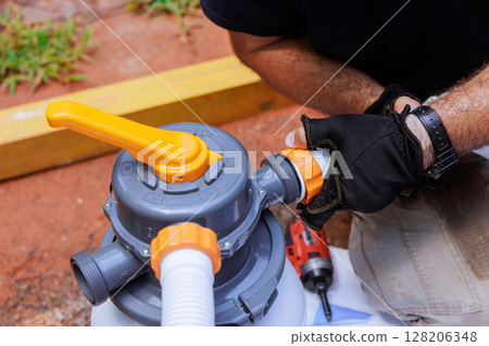 Individual works on connecting parts of pool filter in home backyard, showing tools equipment used. 128206348