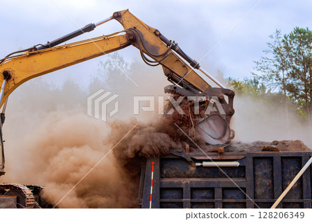 Heavy machinery lifts dirt, debris at construction site while dust clouds rise into air on works day. 128206349