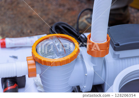 Worker assembles pool pump in an outdoor environment, paying attention to fitting details components. 128206354