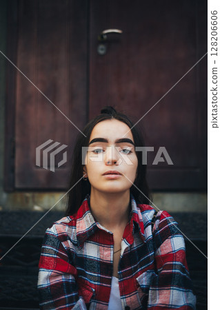 Woman with a plaid shirt and a ponytail is sitting on a staircase 128206606