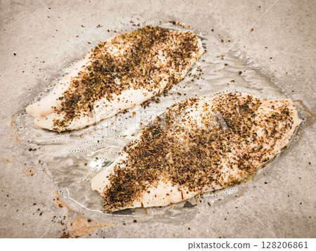 Fresh fish fillets cod seasoned with herbs and spices ready for cooking on a baking sheet showcasing culinary preparation healthy eating concept 128206861