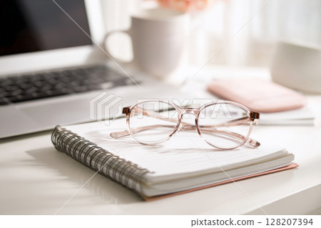 Round eyeglasses on notebook with laptop and coffee mug Round eyeglasses on notebook with laptop and coffee mug 128207394