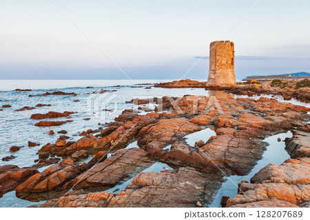 Ancient coastal watchtower on rocky shore at sunset with calm sea and soft twilight sky 128207689