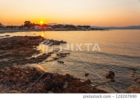 Coastal village shoreline with rocky beach and calm sea during golden summer sunset Coastal village shoreline with rocky beach and calm sea during golden summer sunset 128207690