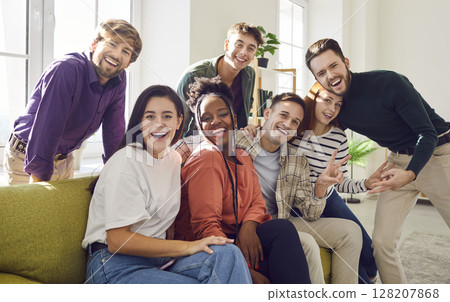 Happy young diverse friends sitting on sofa at home looking cheerful at camera enjoying meeting 128207868