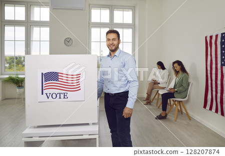 Happy american voter man standing in voting booth on election day at vote center. 128207874