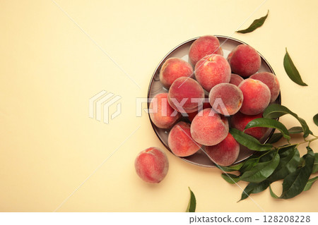 Sweet peaches and leaves on dark plate on beige background. Space for text 128208228