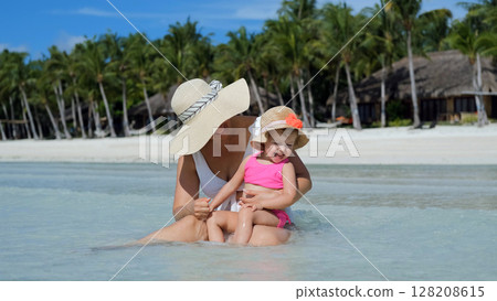 Mom sits in clear ocean water with baby daughter during tropical vacation Mom sits in clear ocean water with baby daughter during tropical vacation 128208615