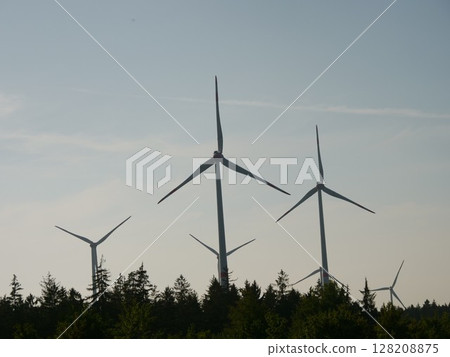 Group of wind turbines are in the sky, with the sun setting behind them 128208875