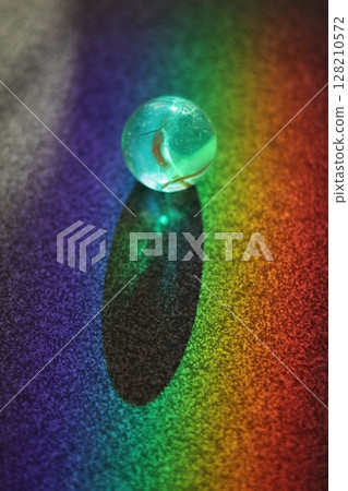 Small, clear, blue ball sits on a colorful surface Small, clear, blue ball sits on a colorful surface 128210572