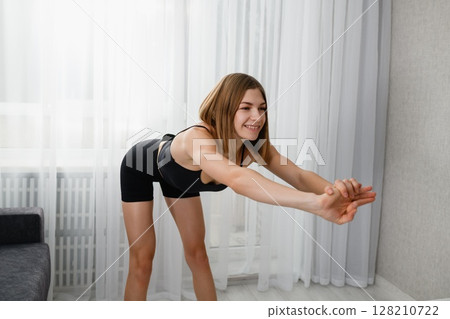 Young woman in black sportswear performing a forward stretch with clasped hands. Young woman in black sportswear performing a forward stretch with clasped hands. 128210722