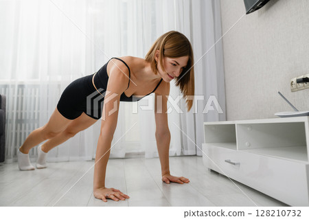 Young woman doing plank exercise on floor at home. Young woman doing plank exercise on floor at home. 128210732