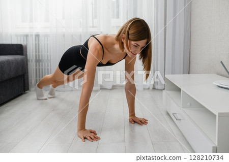Young woman doing plank exercise on floor at home. 128210734