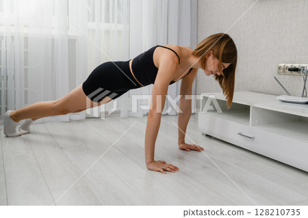 Young woman doing plank exercise on floor at home. 128210735