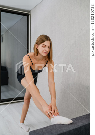 Young woman stretching hamstring with foot on sofa at home. Young woman stretching hamstring with foot on sofa at home. 128210738