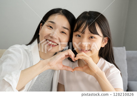 母親和女兒在室內用手做出心形 母親和女兒在室內用手做出心形 128210826