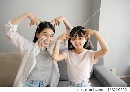 Mother and daughter playing cat ears indoors 128210832
