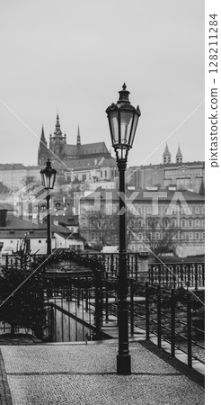 A striking black and white view showcases Prague Castle rising majestically in the background. The street is lined with vintage lamps, enhancing the atmospheric charm of the scene. A striking black and white view showcases Prague Castle rising majestically in the background. The street is lined with vintage lamps, enhancing the atmospheric charm of the scene. 128211284