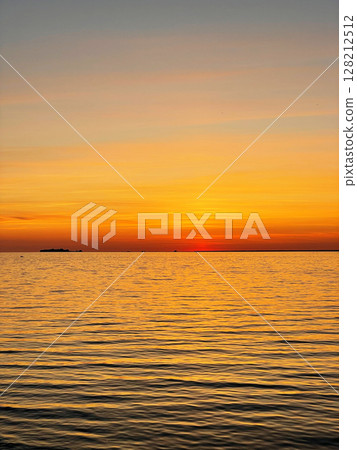 Calm sunset over the sea. The sky is painted with bright colors. Beautiful summer evening at the beach. Vertical photo. 128212512