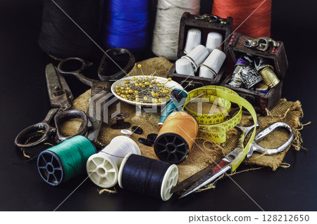 Steel scissors, Spools of thread of various colors, Thimbles in small wooden treasure chest, Sewing needles stuck in a green miniature spools thread and Measuring tape including pins in small round 128212650