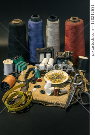Steel scissors, Spools of thread of various colors, Thimbles in small wooden treasure chest, Sewing needles stuck in a green miniature spools thread and Measuring tape including pins in small round 128212651