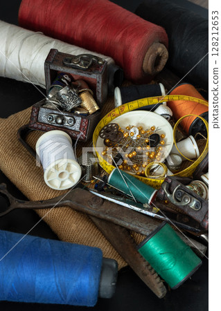Spools of thread of various colors, Thimbles in small wooden treasure chest, Steel scissors, Sewing needles stuck in a green miniature spools thread and Measuring tape including pins in small round 128212653