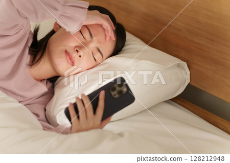 Woman using smartphone in bed at night 128212948