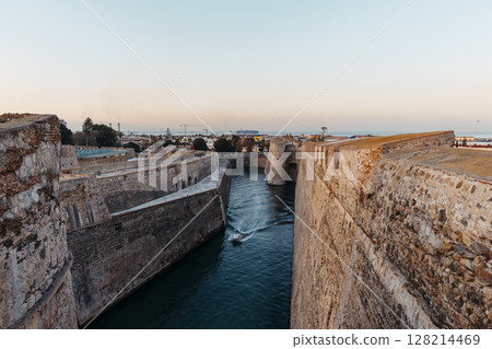 General view of the moat of the Royal Walls of Ceuta at sunset while a ship crosses it General view of the moat of the Royal Walls of Ceuta at sunset while a ship crosses it 128214469